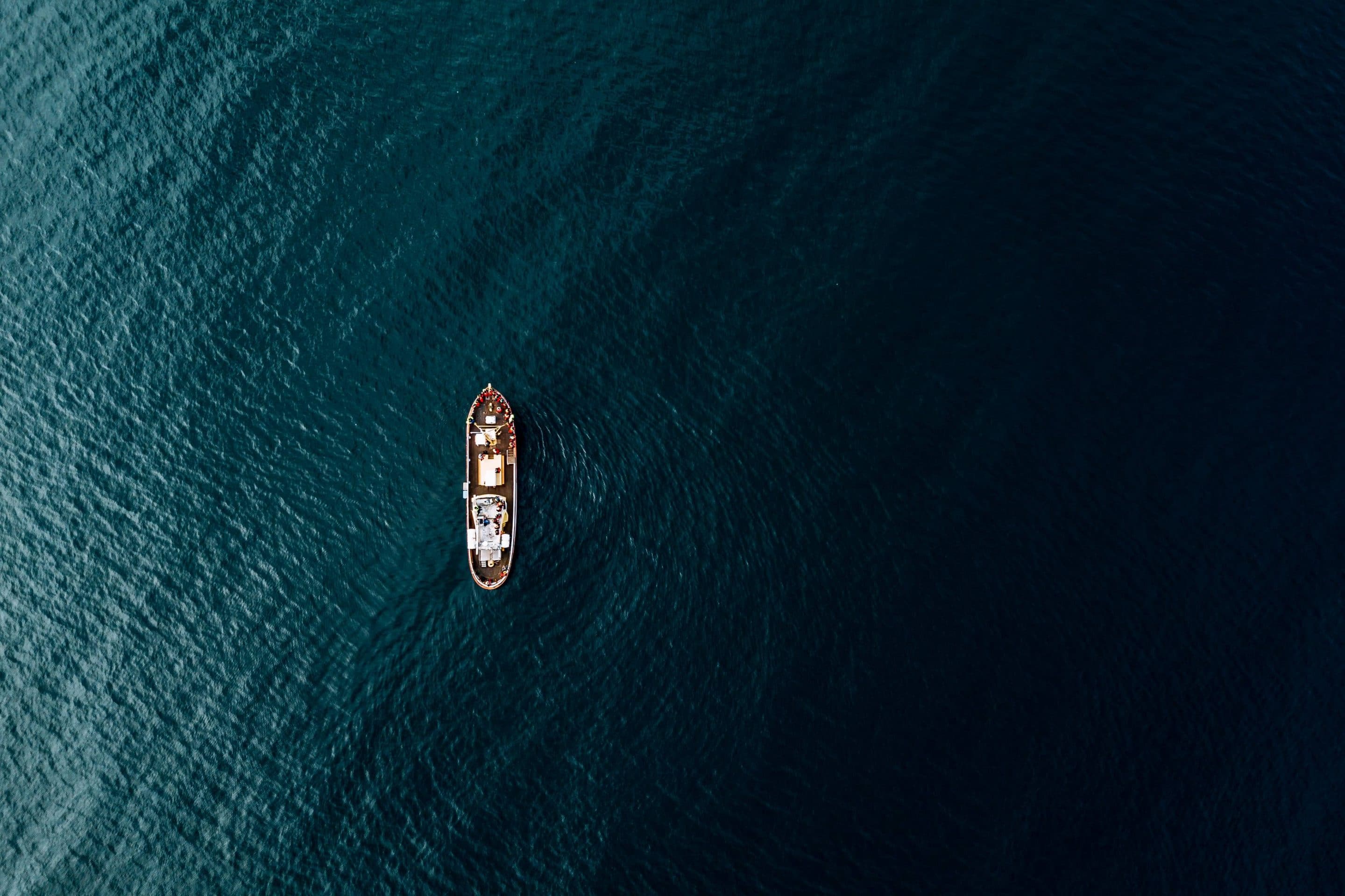 A school of humpback whales captured via drone in the ocean near the Icelandic coast playfully engaging with a ship by photographer Michael Schauer